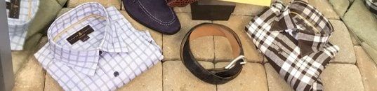 A check dress shirt, a brown suede shoe, a leather belt and a folded brown check shirt laid out on a stone step.