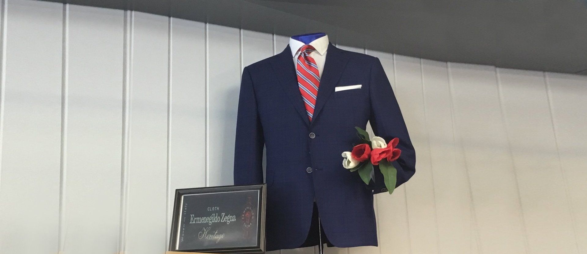 A navy suit on a display form at Mosher's, worn with a red and white striped tie and a white pocket square.