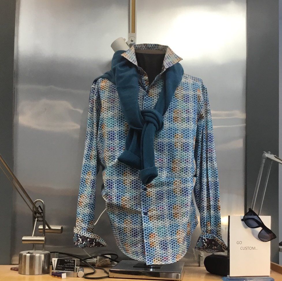 A patterned blue and gold sport shirt on a display form at Mosher's, with a navy scarf at the neck and sunglasses on the plinth.