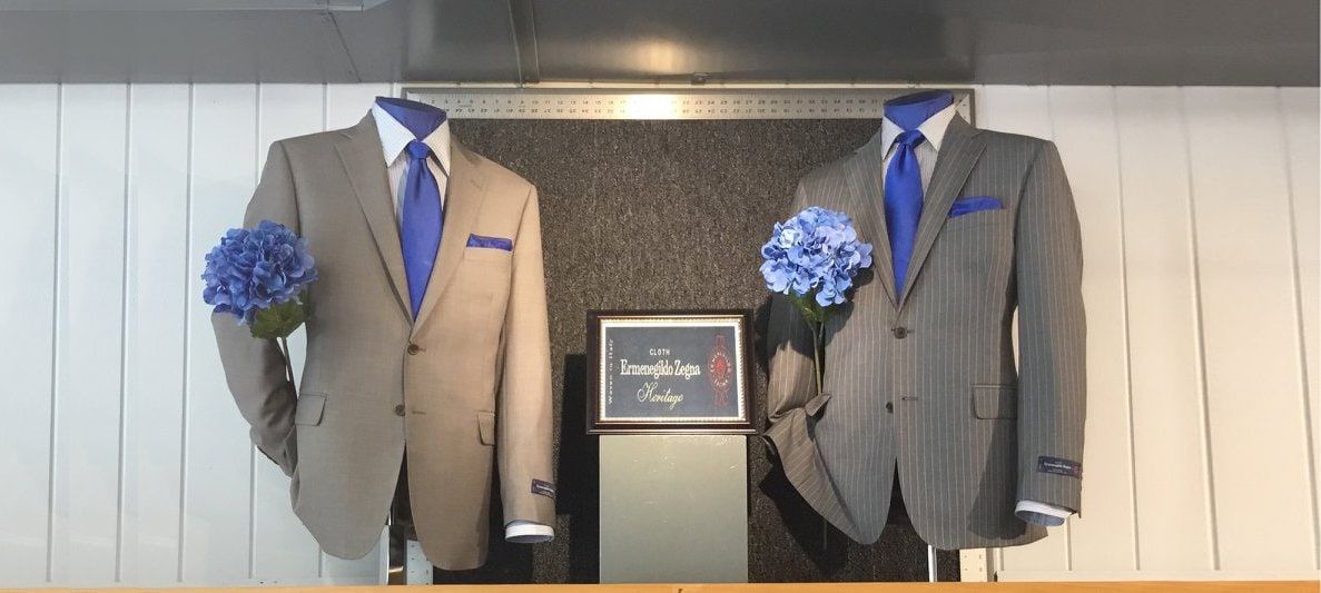Two suits on display forms in the Mosher's window — one tan, one grey pin-stripe — each with a blue tie and a pocket square.