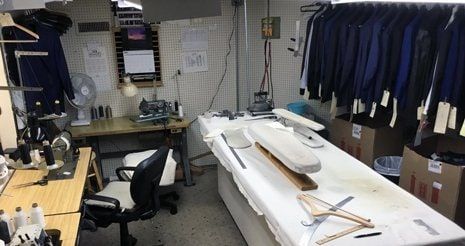 The pressing table in the Mosher's workroom, with shears, chalk and a sleeve board, and finished jackets hanging behind.